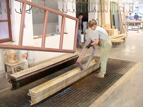Worker dipping wooden window frames into an impregnation and basic coating bath in a workshop
