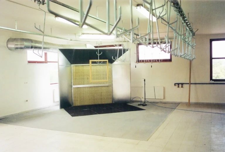 Industrial wood finishing spray booth with overhead hanging rails, ventilation ducting, and an extractor unit in a workshop